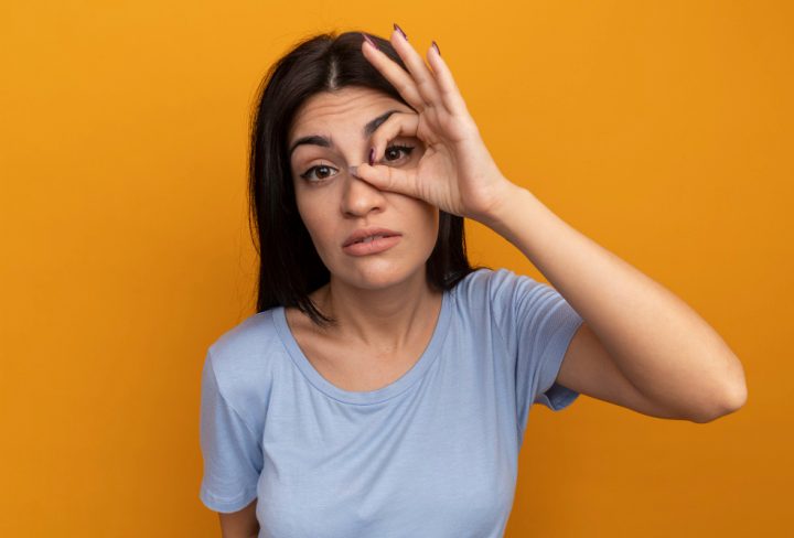 confident-pretty-brunette-caucasian-girl-looks-camera-through-fingers-orange